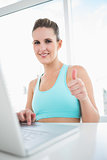 Smiling woman in sportswear using laptop giving thumbs up