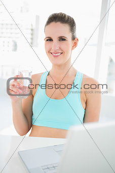 Smiling woman in sportswear holding glass of water