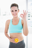 Smiling model in sportswear holding orange slices on her belly