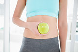 Woman in sportswear holding apple on her toned belly