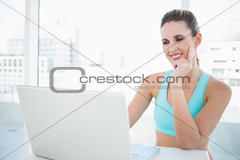 Thoughtful woman in sportswear using laptop