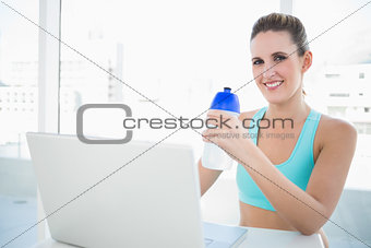 Smiling blonde woman in sportswear holding flask
