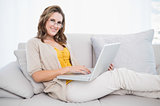 Smiling gorgeous model using laptop on cosy sofa