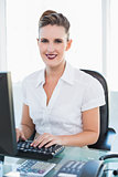 Smiling businesswoman working on computer looking at camera