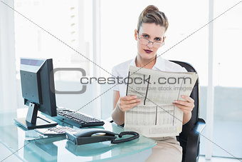 Serious businesswoman wearing glasses holding a newspaper