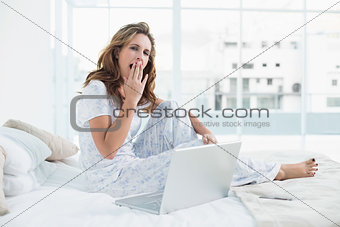 Tired woman sitting on cosy bed with laptop