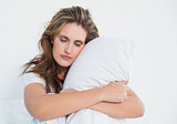 Woman hugging pillow sitting on her bed