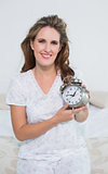 Smiling woman sitting on bed holding alarm clock