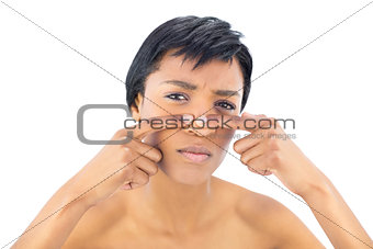 Frowning black haired woman popping a pimple