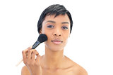 Beautiful black haired woman applying powder on her cheeks