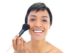 Delighted black haired woman applying powder on her cheeks