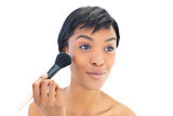 Content black haired woman applying powder on her cheeks