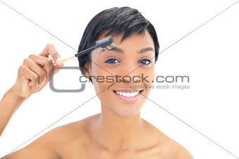 Happy black haired woman brushing her eyebrows