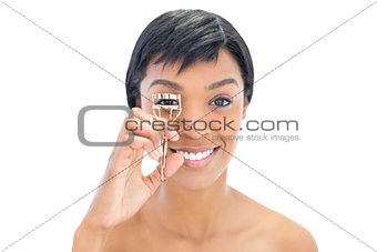 Happy black haired woman using an eyelash curler