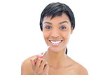 Joyful black haired woman applying gloss on her lips