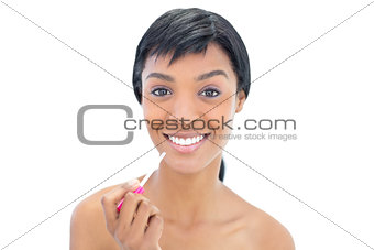 Joyful black haired woman applying gloss on her lips