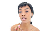 Concentrated black haired woman applying gloss on her lips