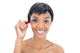 Amused black haired woman applying mascara