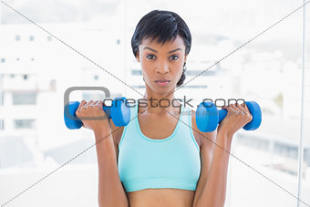 Frowning black haired woman holding dumbbells