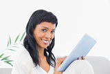 Pleased black haired woman in white clothes typing on a tablet pc
