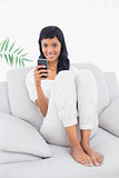 Delighted black haired woman in white clothes typing on her mobile phone