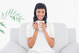 Stylish black haired woman in white clothes enjoying coffee