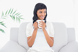 Pensive black haired woman in white clothes enjoying coffee