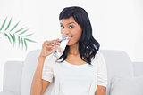 Amused black haired woman in white clothes enjoying a glass of water