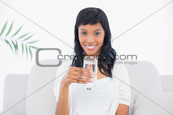 Delighted black haired woman in white clothes drinking water