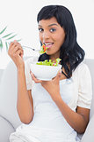Calm black haired woman in white clothes eating salad