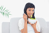 Relaxed black haired woman in white clothes eating salad