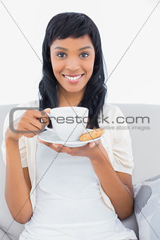 Pleased black haired woman in white clothes drinking coffee