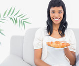 Charming black haired woman in white clothes holding a croissant