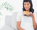 Amused black haired woman in white clothes smelling a croissant