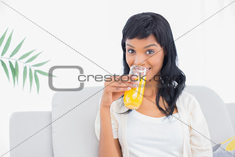 Charming black haired woman in white clothes drinking orange juice