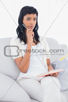 Pensive black haired woman in white clothes writing on a notebook
