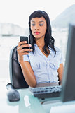 Unsmiling businesswoman looking at her mobile phone