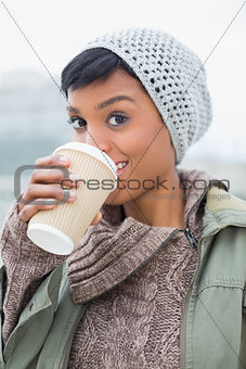 Pleased young model in winter clothes enjoying coffee