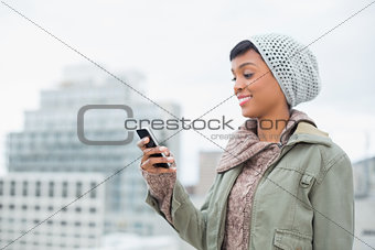 Amused young model in winter clothes looking at her mobile phone