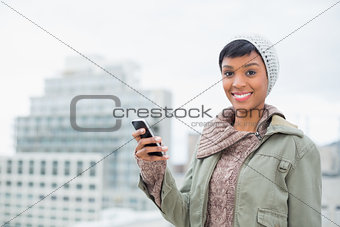 Cheerful young model in winter clothes holding her mobile phone
