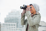 Smiling young model in winter clothes watching with binoculars