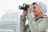 Pretty young model in winter clothes watching the city with binoculars
