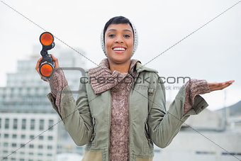 Pleased young model in winter clothes holding binoculars