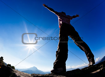 Man opens his arms in the sunshine against blue sky. 