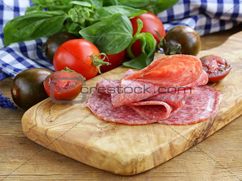 smoked sausage, tomatoes and basil on a wooden cutting board