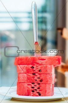 Watermelon slices are stacked on a silver platter and they stuck a table knife.