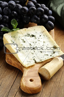 piece of blue cheese with grapes on a wooden board