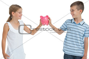 Smiling brother and sister holding piggy bank together