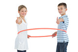 Happy brother and sister playing with hula hoop giving thumbs up