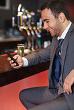 Smiling businessman sending a text while having a drink